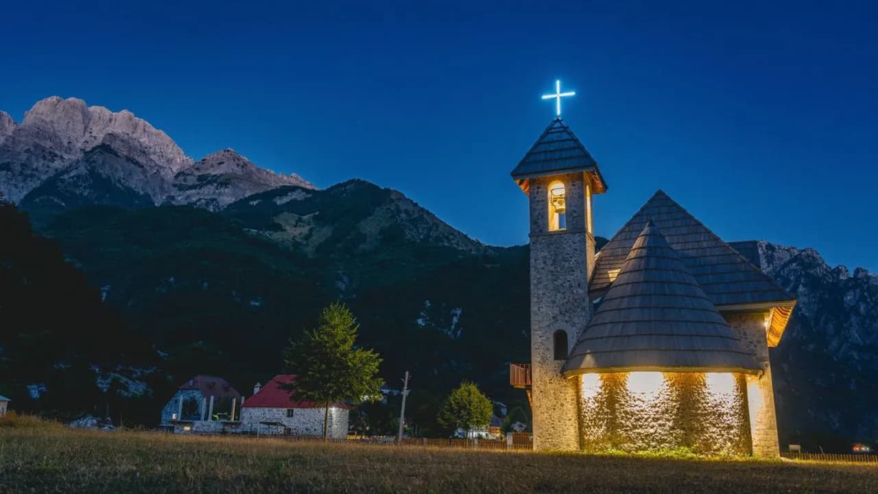 A stone church in the village of Theth, Albania, lit up at dusk beneath the Accursed Mountains
