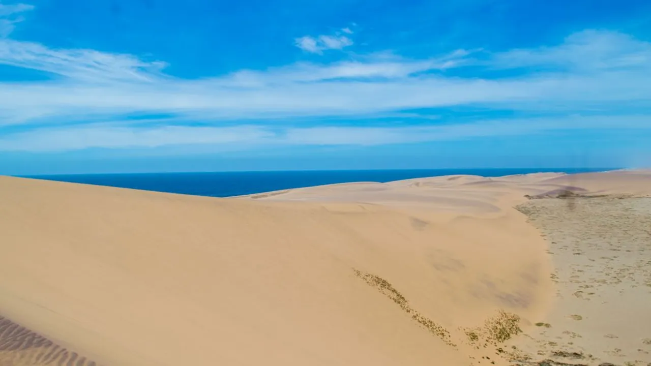 Desert dunes meeting the Atlantic Ocean along a remote coastline, the same landscape where the Namib Desert reaches Angola's southern coast near Namibe