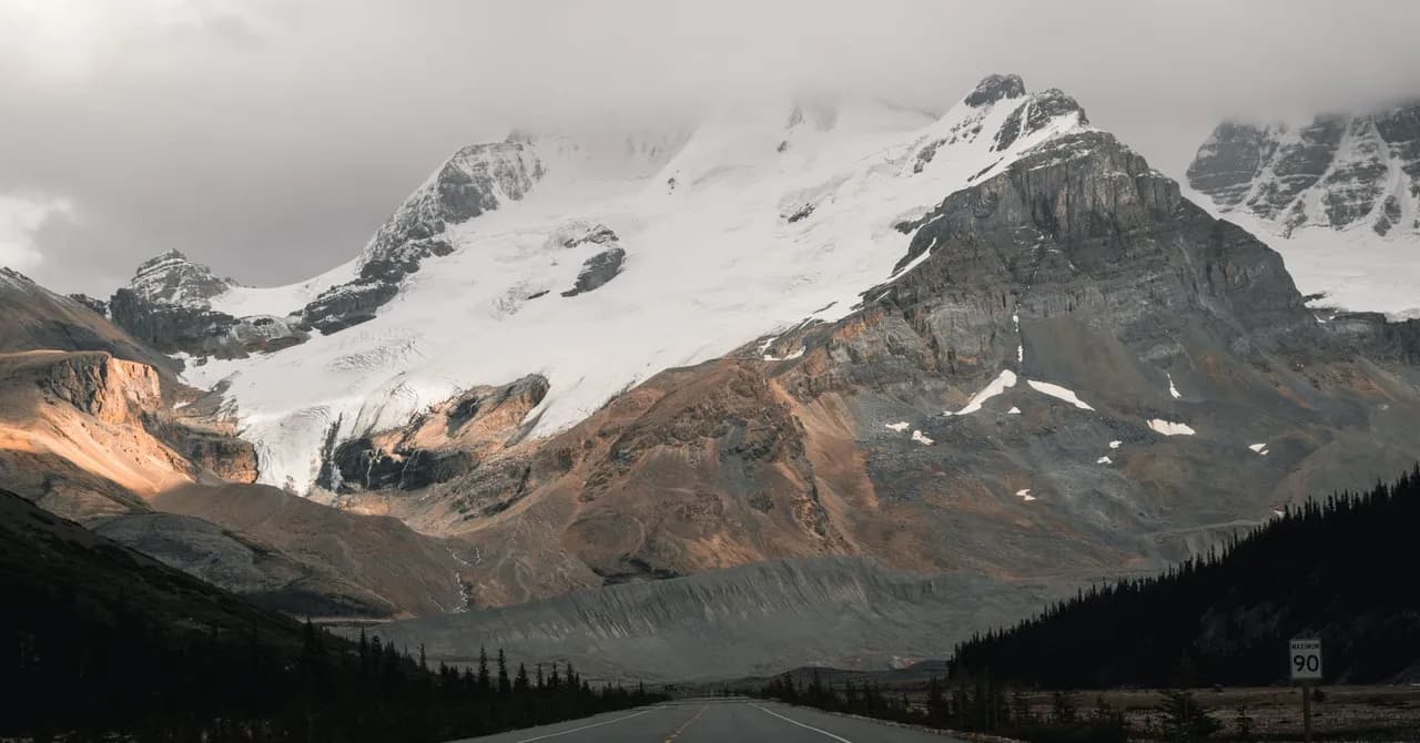 A two-lane highway running toward snow-capped mountains on the Icefields Parkway near Jasper, Alberta