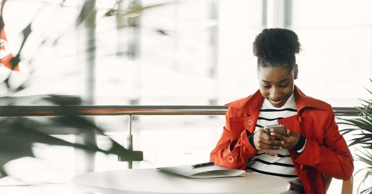 A traveler checking her phone at a café table with a laptop open beside her