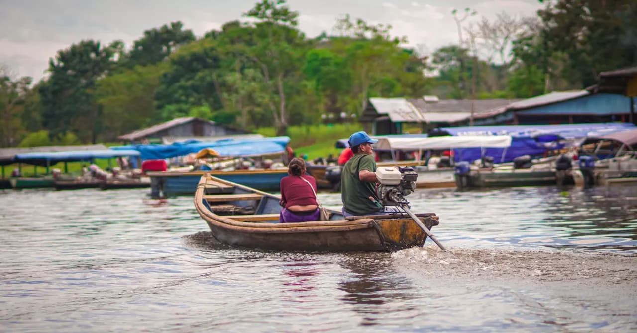 A small boat navigating a wide river through dense rainforest