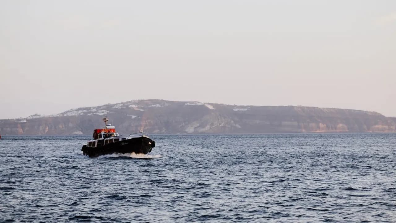 A ferry boat sailing past the whitewashed cliffside town of Santorini, Greece