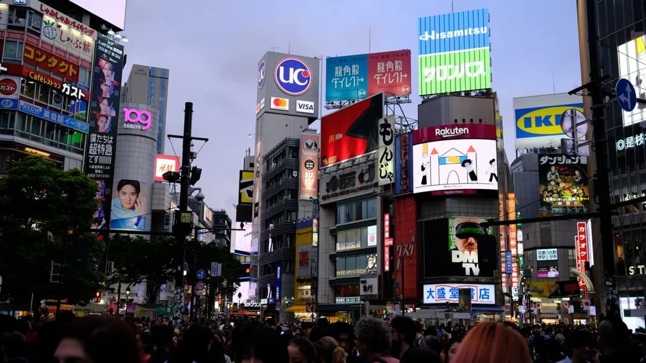 Crowds crossing the intersection at Shibuya in Tokyo at night, under neon advertising screens