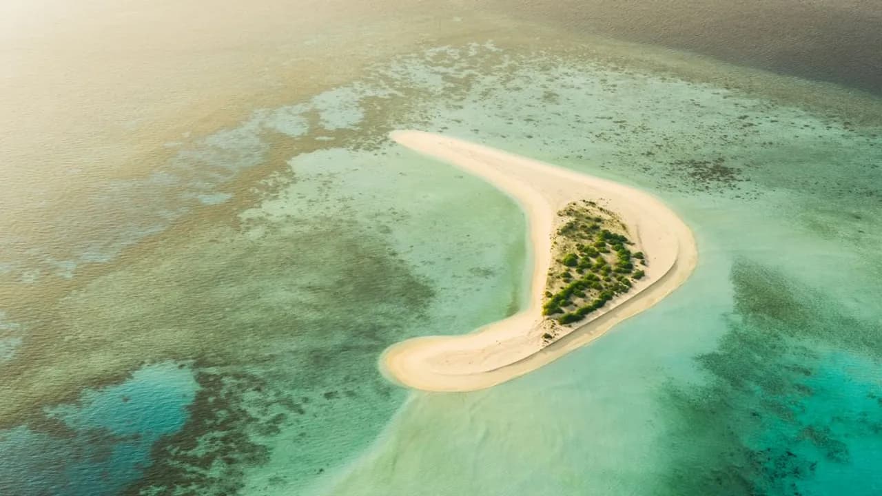 Aerial view of turquoise water and a coral reef surrounding a small island in the Maldives