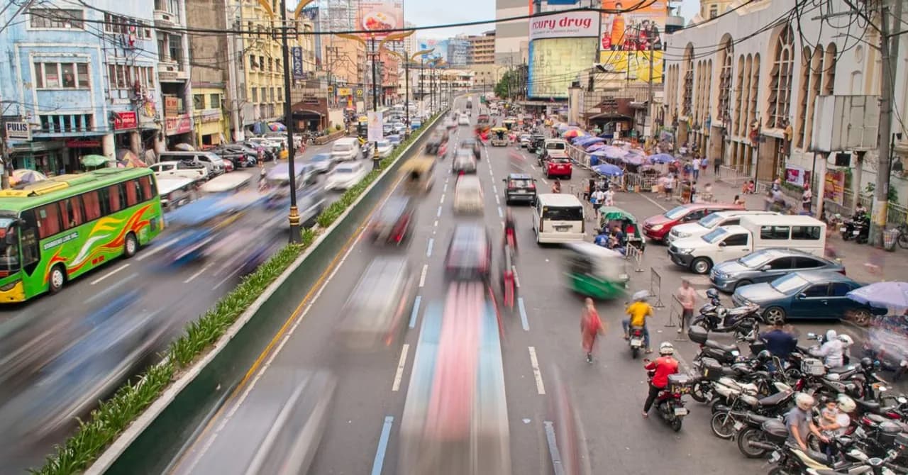A busy Manila street seen from above, packed with jeepneys, buses, motorbikes and market umbrellas in dense traffic