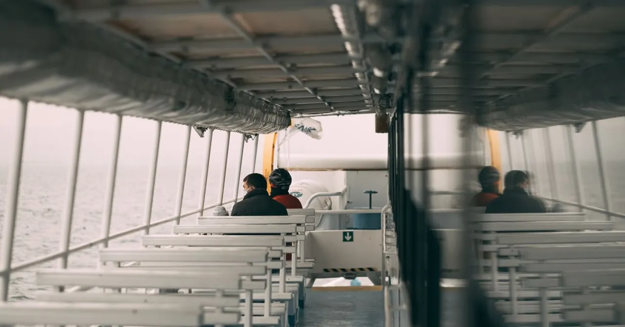 Passengers on the open upper deck of a ferry, with nothing but open sea on the horizon