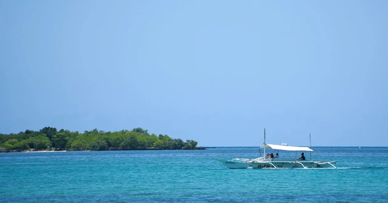A Philippine outrigger banca carrying passengers across open turquoise water toward a low forested island
