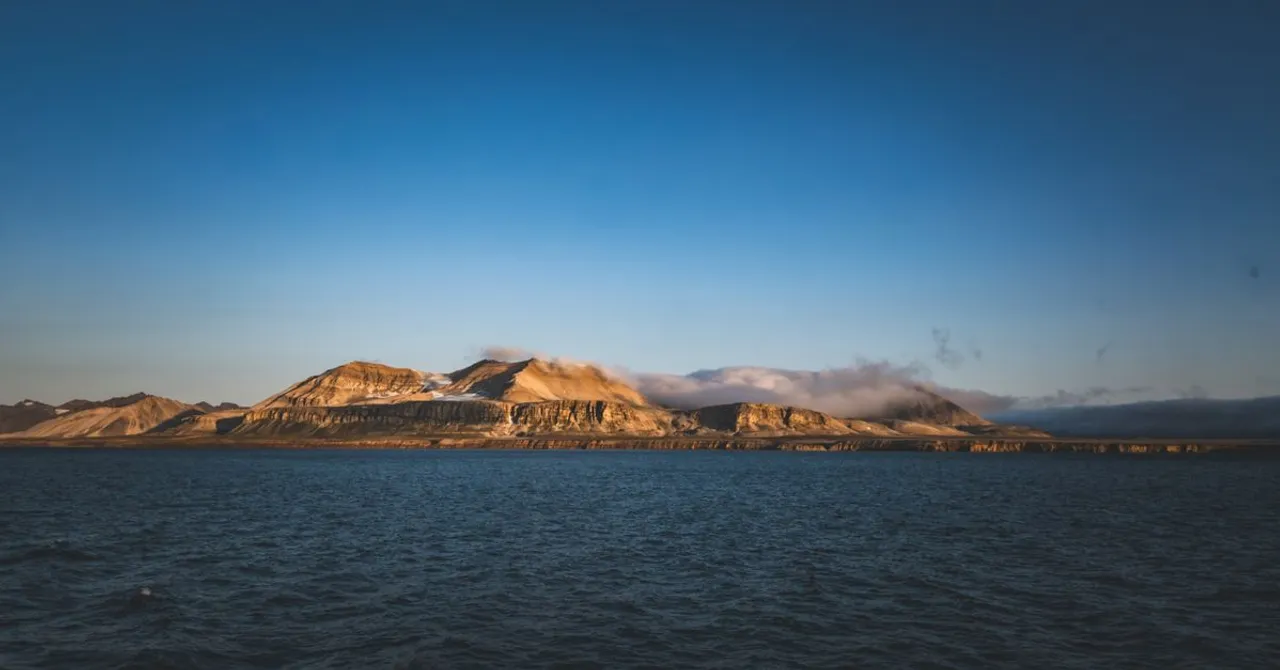 A bare, flat-topped arctic coastline seen from the water under a clear sky