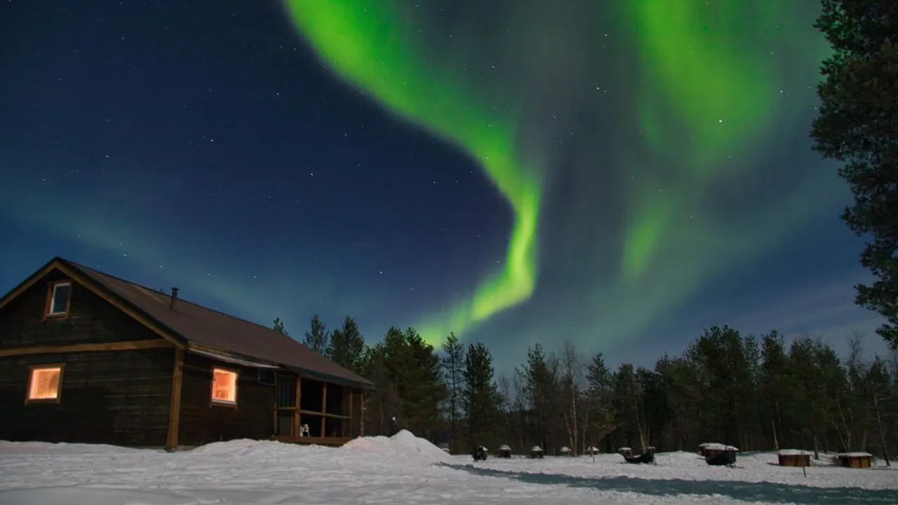The green aurora borealis glowing over a snow-covered log cabin in Swedish Lapland near Kiruna