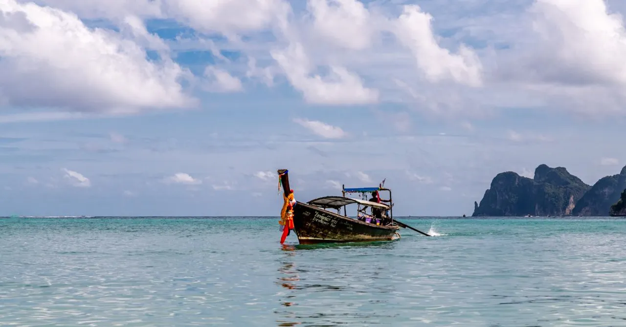 A traditional Thai longtail boat anchored in the turquoise water of the Andaman Sea near a limestone island