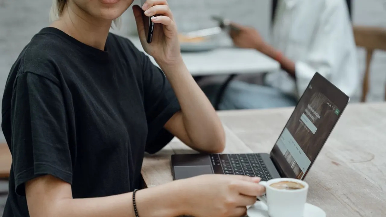 A traveler at a cafe table with a laptop and phone, the kind of public Wi-Fi setting a VPN was originally built to protect