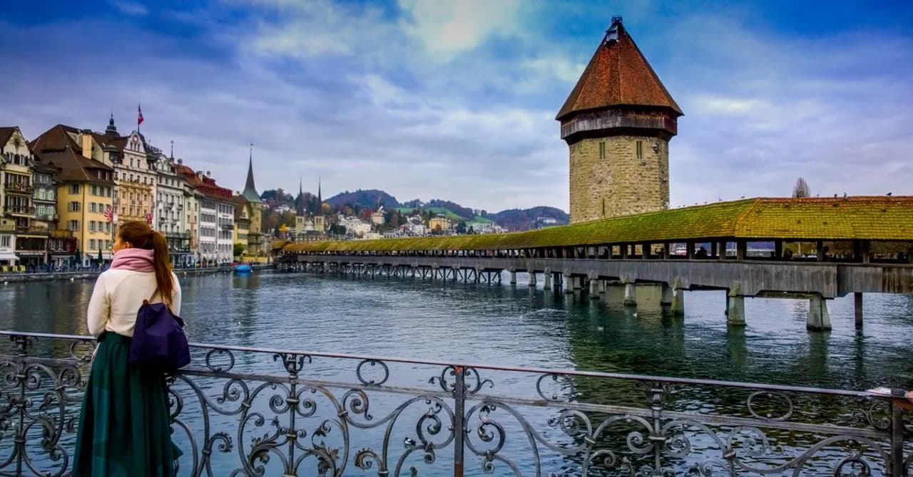 Eine hölzerne überdachte Brücke und ein steinerner Wasserturm über einem Fluss vor einer Altstadt